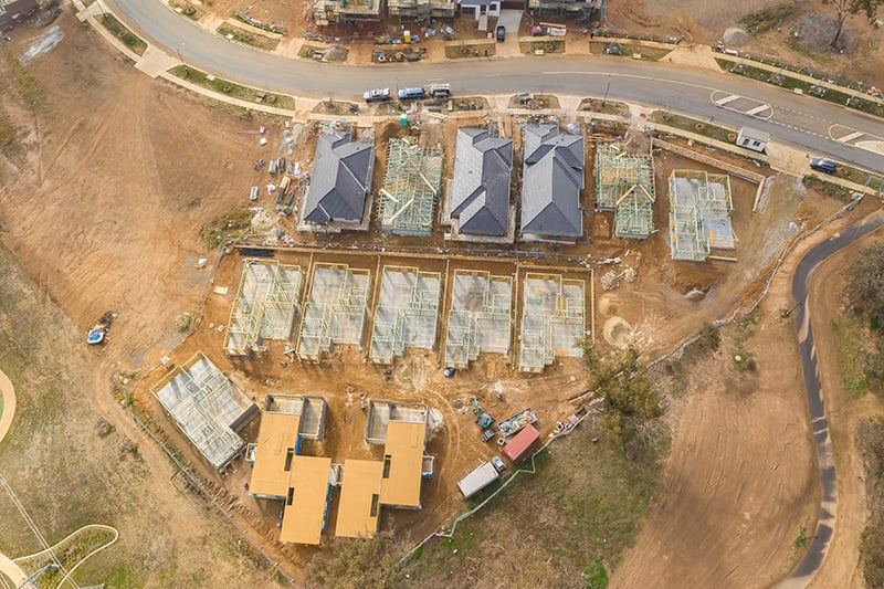 Aerial drone view of residential housing development under construction showing multiple homes at various build stages, from slab and framing to roofing completion