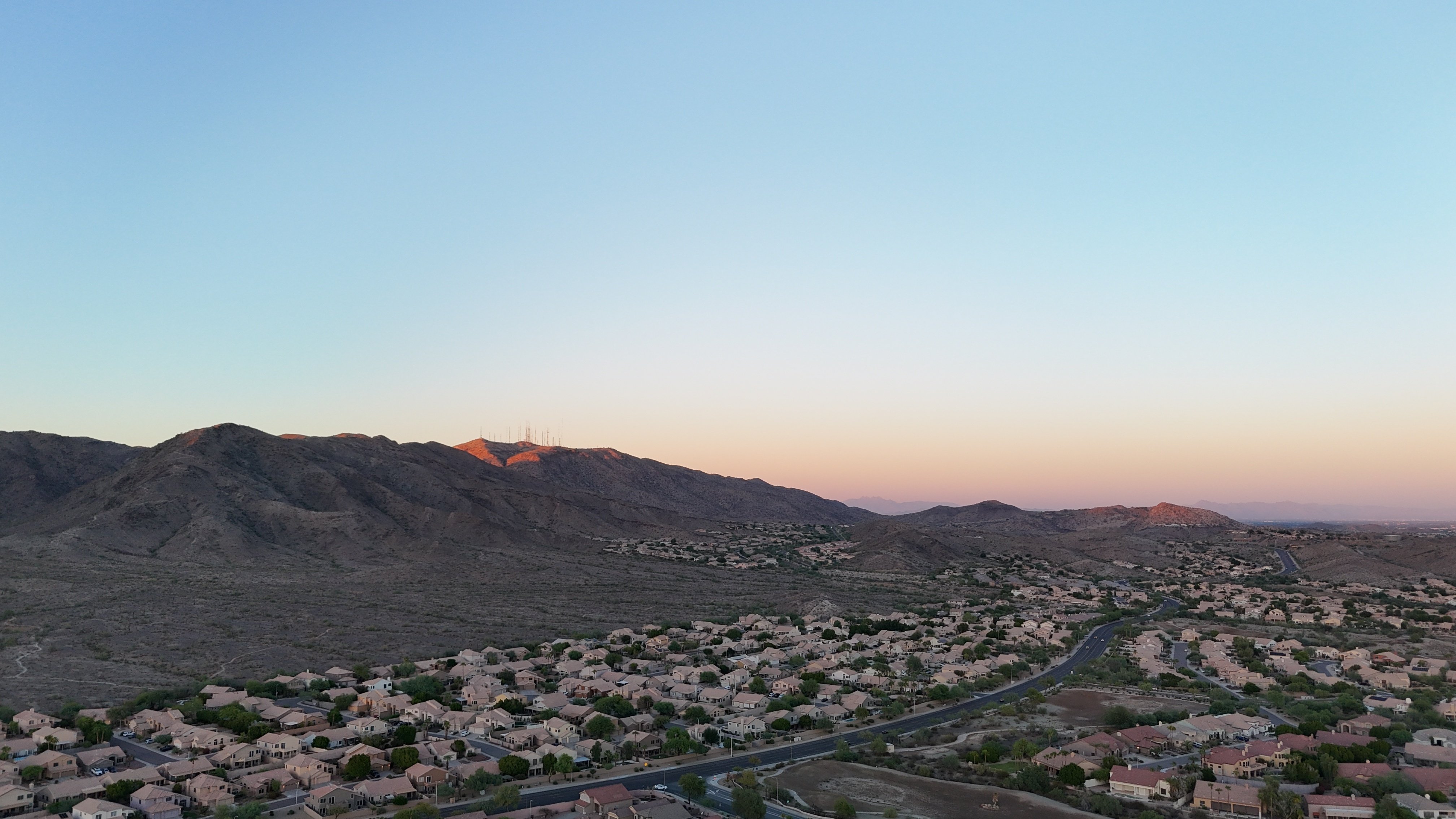 Aerial view of suburban residential development at the edge of a desert mountain range in a Western growth corridor, illustrating peri-urban transitional land acquisition near Phoenix, San Antonio, or Boise