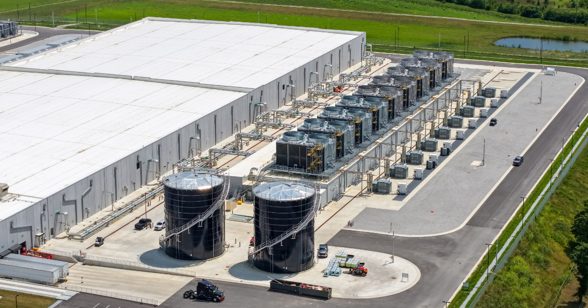 Aerial view of an industrial data center facility with cooling towers and bulk water storage tanks, highlighting cooling water access and utility infrastructure.